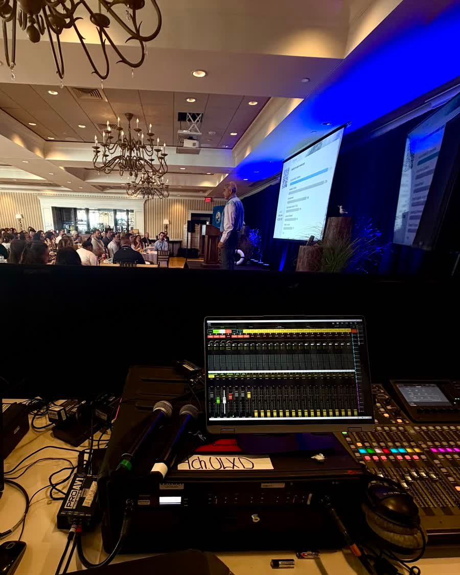 A mixing console at front of house, with the stage and a full room beyond